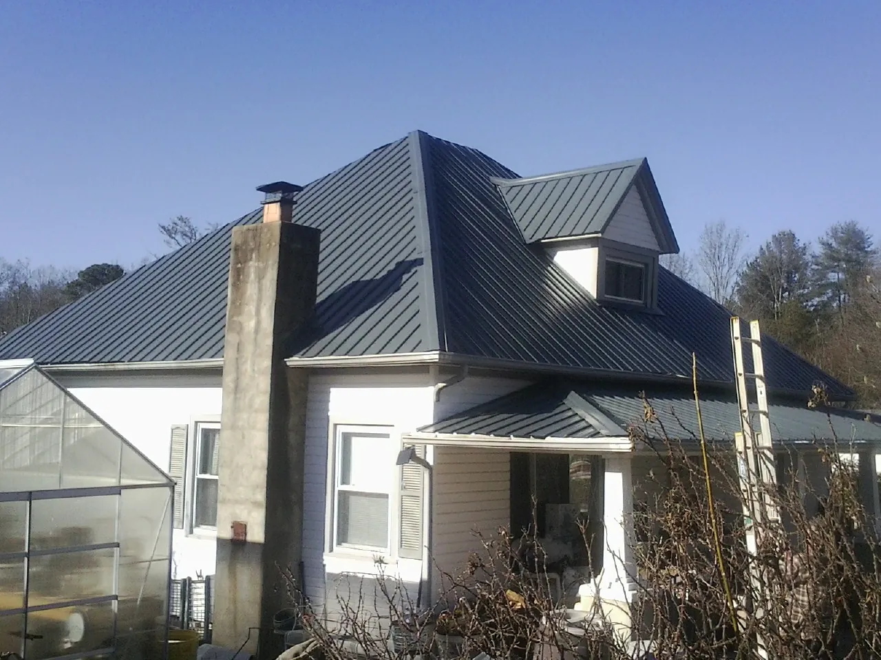 Dark blue standing seam metal roof on a white farmhouse with dormer — Slate & Tile Roof Repair by Roofing Brothers in Gentryville