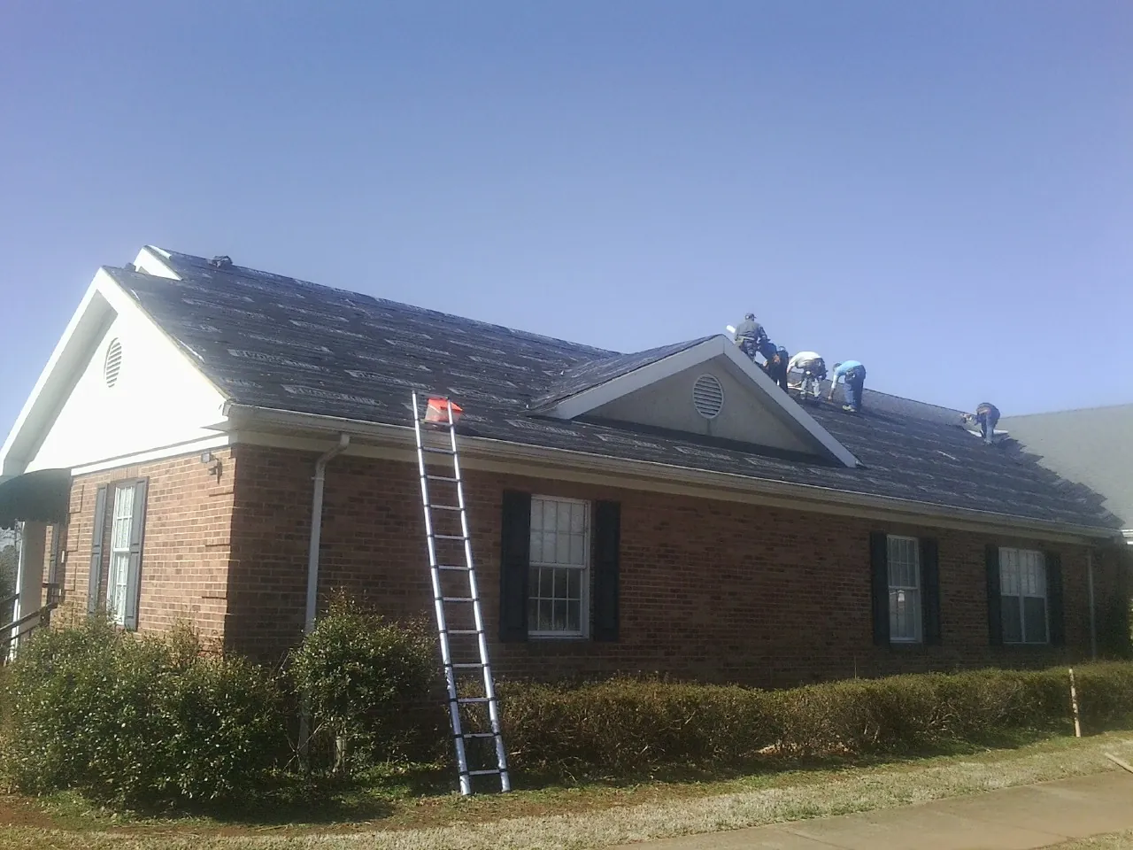Crew tearing shingles off a brick ranch roof with a ladder set — Emergency Roof Repair work by our crew in Gentryville