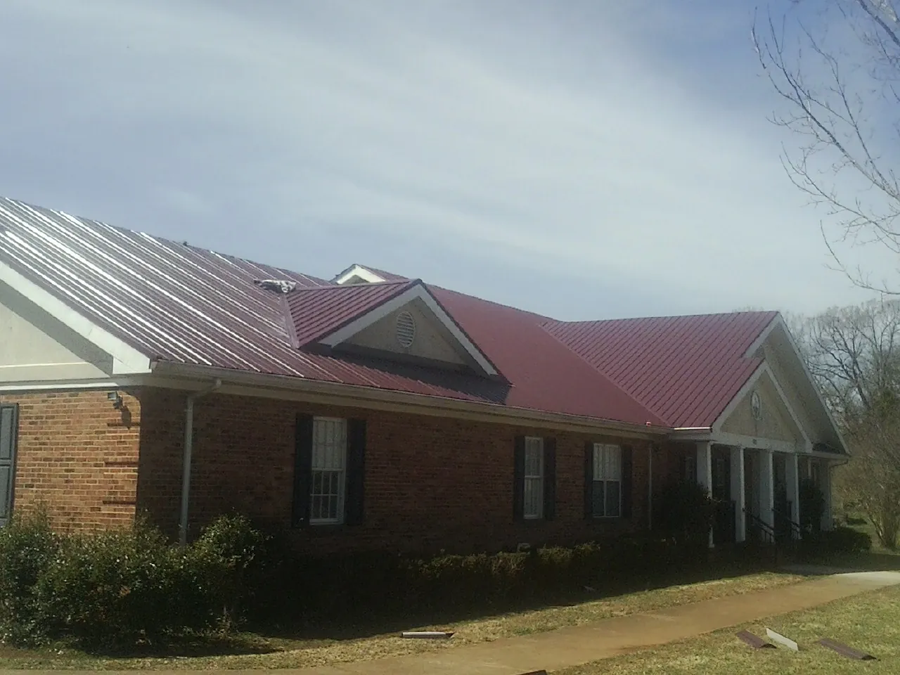 Red metal roof with gabled entries on a long brick building, from a Hail Damage Roof Repair job in Gentryville