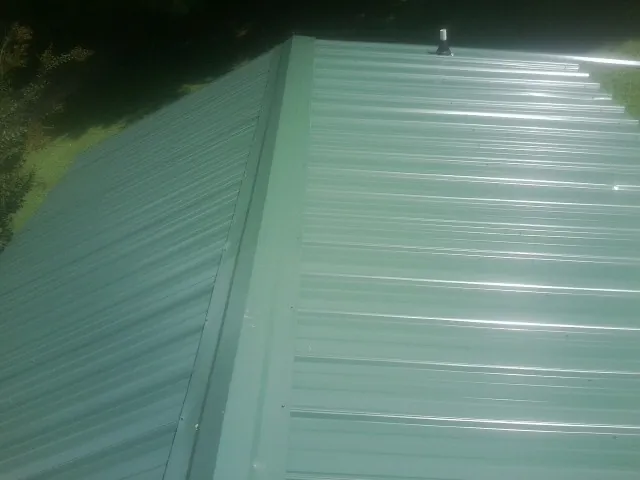 New green metal panels meeting at the ridge of a roof — Flat Roof Repair work by our crew in Gentryville