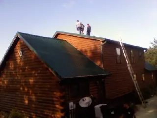 Crew on the ridge of a green metal roof on a two story log home in Gentryville