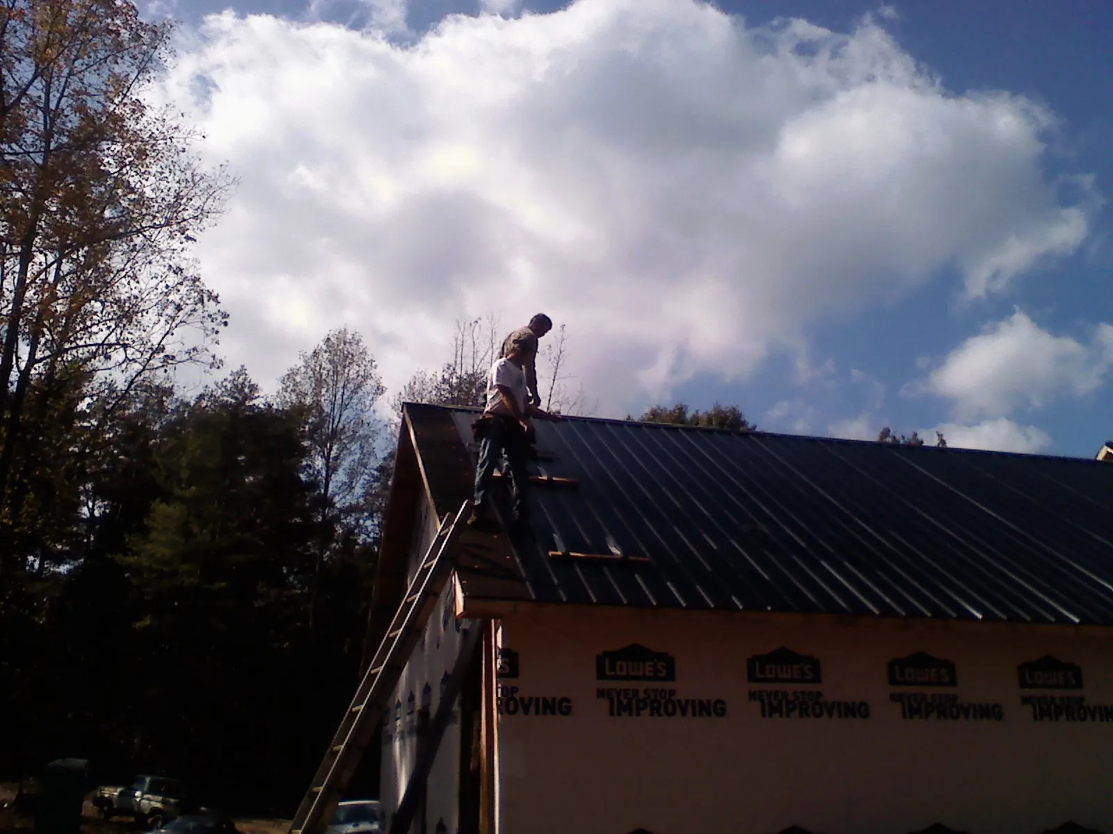 Roofer fastening dark metal panels high against a cloudy sky, from a Roof Inspection job in Gentryville