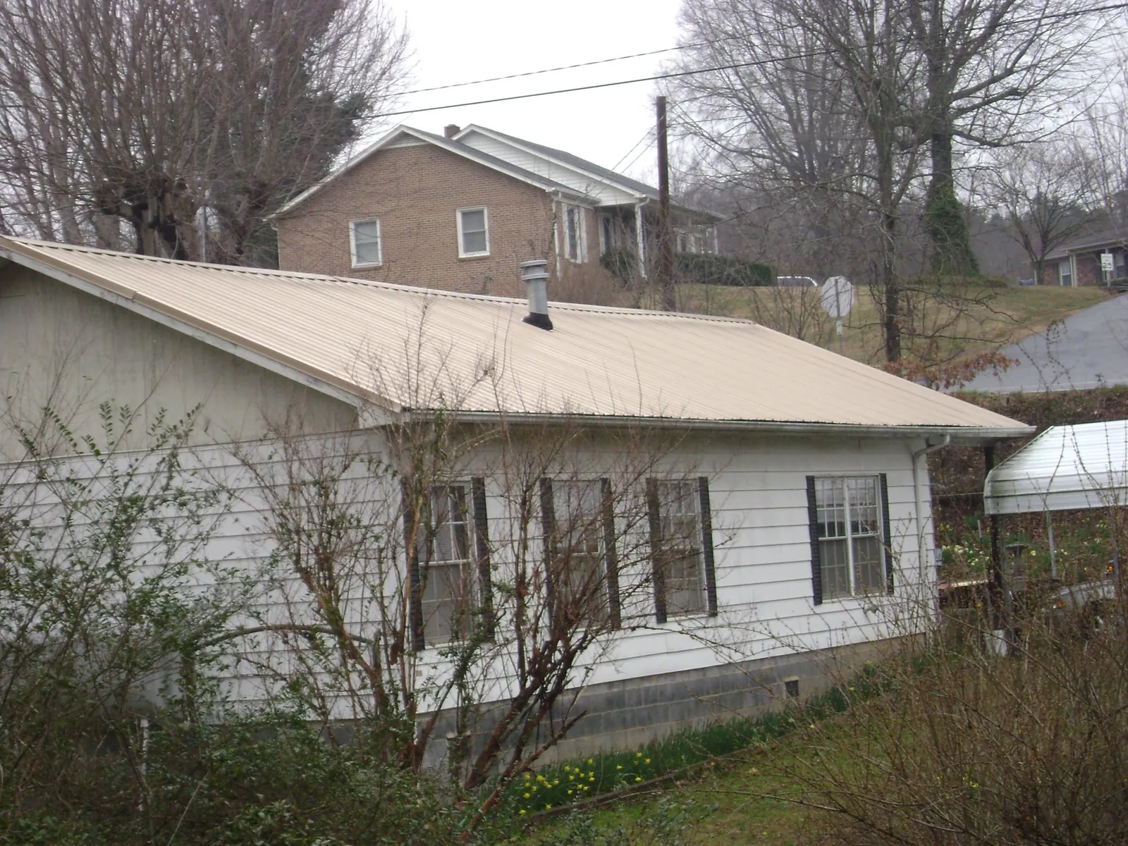 Tan metal roof on a white sided house set into a hillside — Commercial Roofing by Roofing Brothers in Gentryville