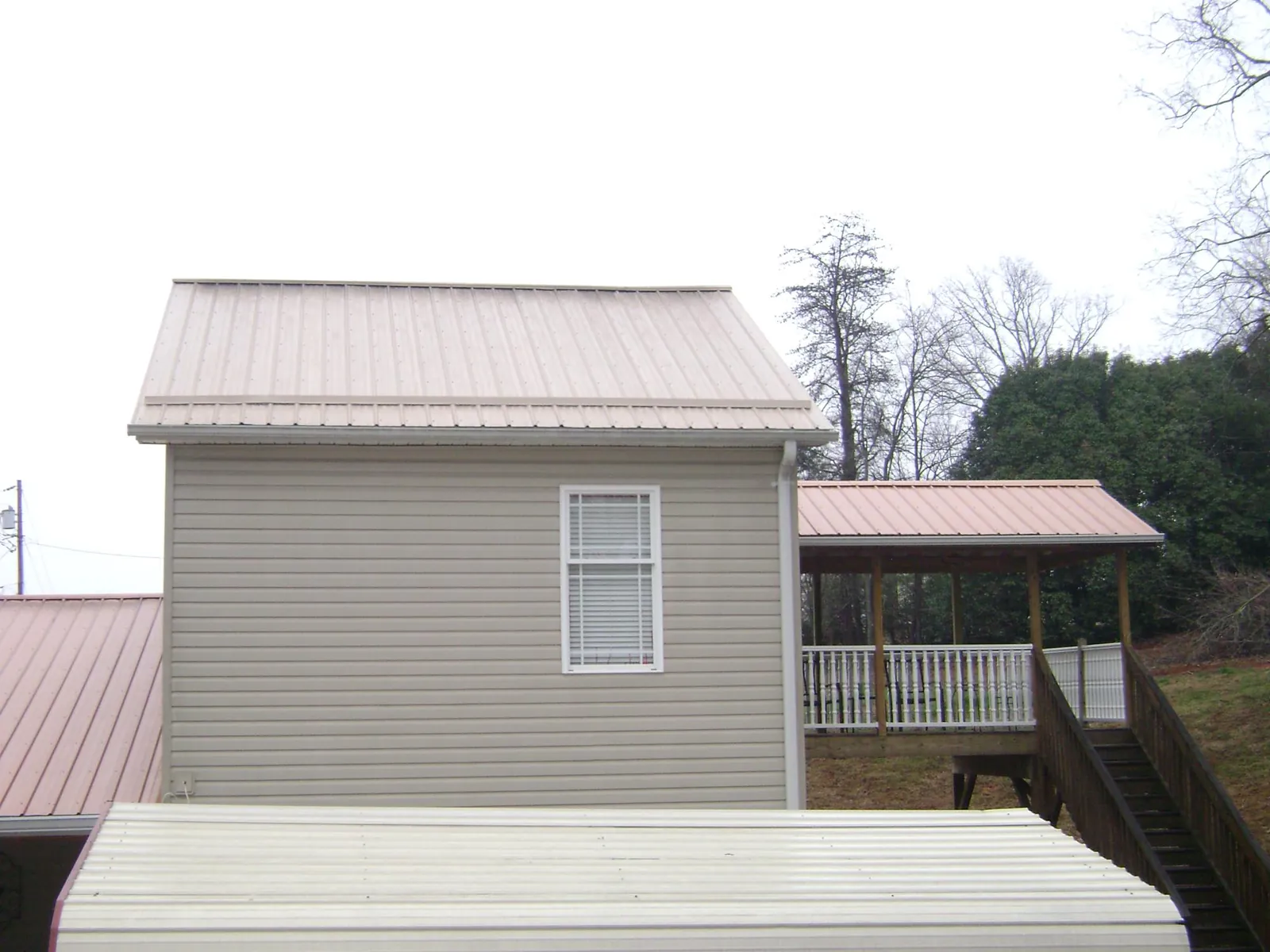 Tan metal roofs on a two story addition and attached porch, from a Roof Replacement job in Gentryville